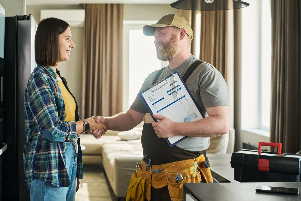 Repairman holding clipboard and invoice talking with homeowner in modern living room — giving an in-home estimate